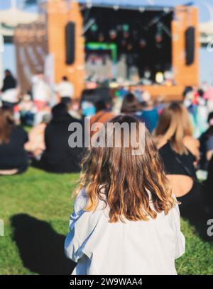 Crowded open air festival concert with scene lights with musicians band on stage at the venue, rock show performance, with concert-goers attendees, au Stock Photo