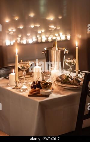 holidays, romantic date and celebration concept - close up of festive table serving for two with champagne bottle in ice bucket and candles burning at Stock Photo