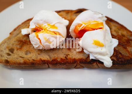 Two broken poached eggs with golden yolks on a slice of buttered toasted crispy sourdough bread. Stock Photo