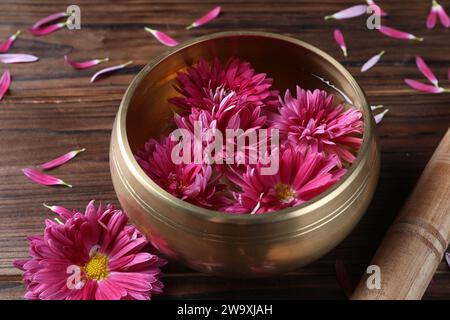 Tibetan singing bowl with water, beautiful flowers and mallet on wooden table, closeup Stock Photo