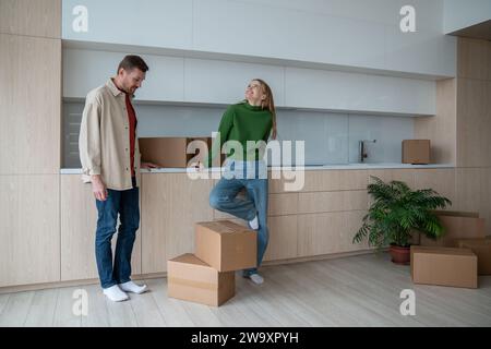 Merry glad couple standing in own new spacious apartment among cardboard boxes on relocation day Stock Photo