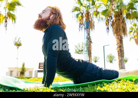 handsome redhaireb man with long beard wear black sporty suit doing yoga meditation in sunny beach Stock Photo