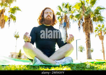 handsome redhaireb man with long beard wear black sporty suit doing yoga meditation in sunny beach Stock Photo