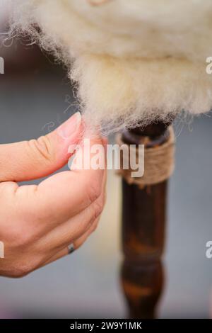 The woman is using a retro spinning to create beautiful yarn from wool. Close-up of a woman's hands knitting wool Stock Photo