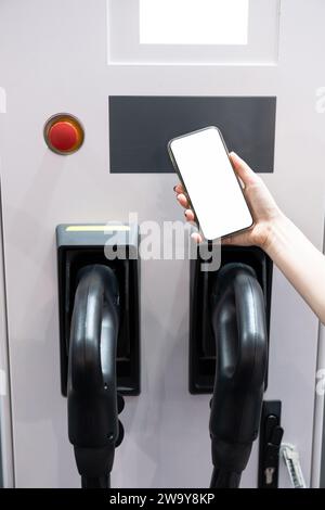Hands with smartphone and charging plug on a background of electric car . White screen, you can add your content here. Stock Photo