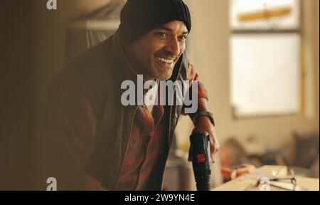Happy DIY carpenter remodeling his kitchen for a home renovation project. He is using a drill gun and working to upgrade the interior. Skilled man smi Stock Photo