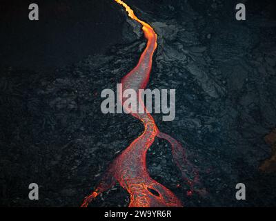 Mesmerizing view of a lava flow, red hot molten liquid streaming over black solid volcanic rocks, aerial directly above shot. Abstract, texture, and Stock Photo