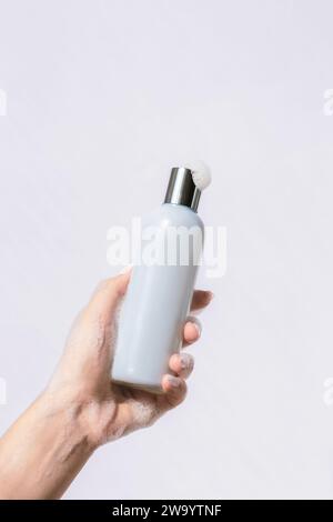 Woman's soapy hand holding cosmetic blue bottle. Natural cosmetics concept. Mockup. Stock Photo