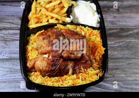 Arabic Syrian cuisine of machine grilled barbecued chicken with colorful Basmati rice and French fries finger potatoes served in a black disposable pl Stock Photo