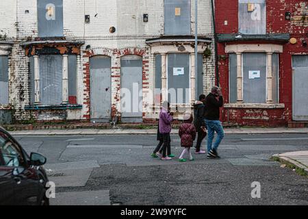 Family of immigrants passing rundown boarded Up, sealed and empty Terraced Property, house, terrace in Liverpool . Stock Photo