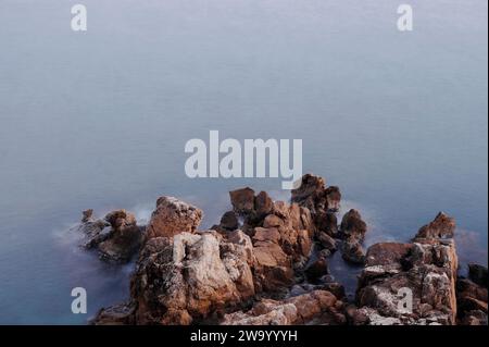 Antibes, France. December 30, 2023. Sea rocks photographed at sunset in front of the medieval walls of Antibes Stock Photo