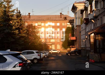 A building in the city is flooded with sunshine and a summer street with cars. Windows in the sun. Stock Photo