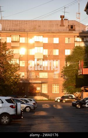 A building in the city is flooded with sunshine and a summer street with cars. Windows in the sun. Stock Photo