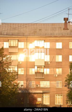 A building in the city is flooded with sunshine and a summer street with cars. Windows in the sun. Stock Photo