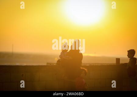 Rafah, Palestinian Territories. 31st Dec, 2023. A displaced Palestinian family, who fled their homes due to Israeli raids, watch the sunset in a camp on New Year's Eve 2024. Credit: Mohammed Talatene/dpa/Alamy Live News Stock Photo