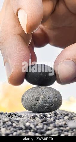 Hand of man places black stone on gray stone creating a pyramid, zen concept, vertical frame. Stock Photo