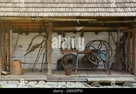 Collection of planers and retro wood saws hang on a wooden wall near an old house. Carpenters plane and other things on the wall Stock Photo