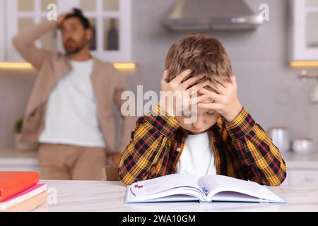 Father getting annoyed while son doing his homework in kitchen, selective focus. Dyslexia problem Stock Photo