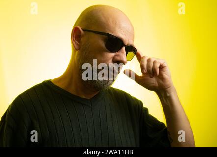 White man, bald, wearing sunglasses, serious and thoughtful. Isolated on yellow background. Stock Photo