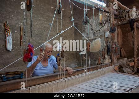 An older man works on horizontal loom in weaving workshop. Kashan, Iran. Stock Photo