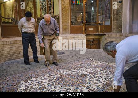 Two sellers accurately check the actual size of an expensive Persian carpet before finalizing a sale in the Grand Bazaar of Kashan, Iran. Stock Photo