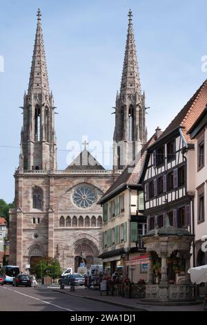 Church with two towers of Saints Peter and Paul and on the right the six bucket water well in Renaissance style in the city center of Obernai, France Stock Photo
