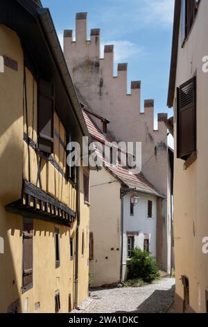 Narrow street in the picturesque French village of Riquewihr with plastered half-timbered houses and a house with battlements on the facade Stock Photo
