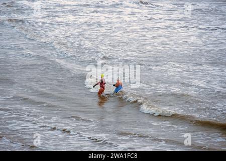 Hastings, East Sussex, UK 1st January 2024. Two intrepid bathers brave the cold early morning sea at Hastings Harbour, on a grey New Years Day. Carolyn Clarke/Alamy Live News Stock Photo