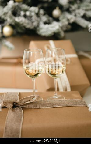 Two wine glasses on wrapped holiday present by christmas tree Stock Photo