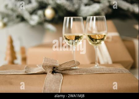 Present wrapped in ribbon with two wine glasses by christmas tree Stock Photo