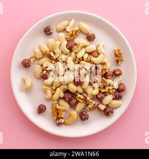 a variety of peeled nuts on a white plate, on a pink background Stock Photo