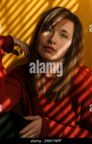 Woman in Orange sweater in front of yellow wall Stock Photo