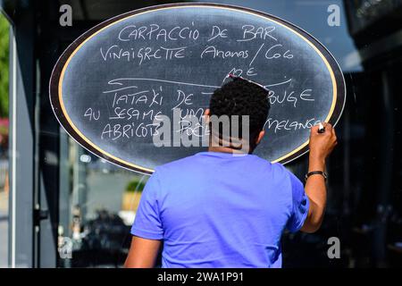 A commis modifying the menu on the sign at the entrance of the restaurant in Amiens | Un commis modifie le menu sur le panneau a l'entree  du restaura Stock Photo