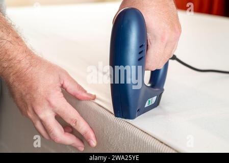 Worker stapling sofa lining with electric staple gun Stock Photo