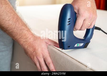 Worker stapling sofa lining with electric staple gun Stock Photo