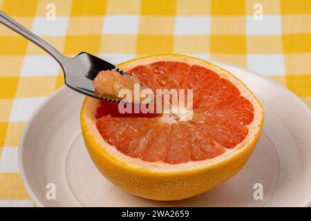 Sliced grapefruit on plate with serrated spoon. Organic fruit, healthy diet and nutrition concept. Stock Photo