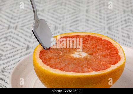 Sliced grapefruit on plate with serrated spoon. Organic fruit, healthy diet and nutrition concept. Stock Photo