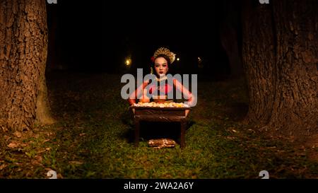 a female dancer looks focused on her ritual with a peaceful facial expression in front of offerings that look fresh and lively at night Stock Photo