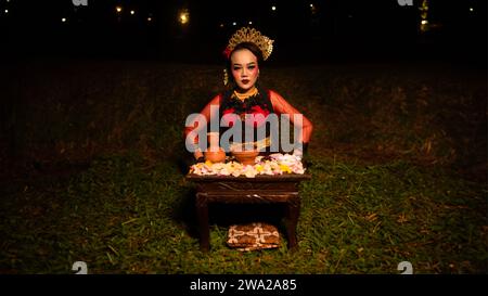 a female dancer looks focused on her ritual with a peaceful facial expression in front of offerings that look fresh and lively at night Stock Photo