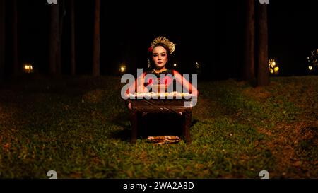 a female dancer looks focused on her ritual with a peaceful facial expression in front of offerings that look fresh and lively at night Stock Photo