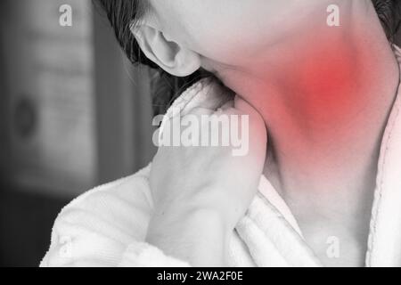 A girl holds her hands behind her neck at home in a dressing gown, her neck hurts, acute pain in the neck Stock Photo