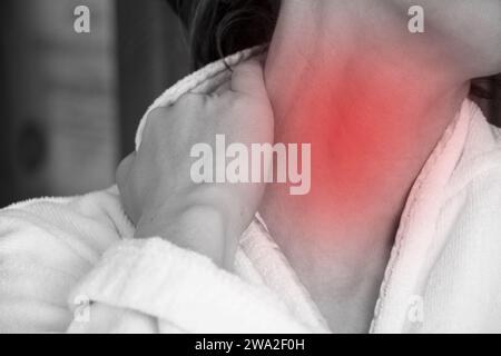 A girl holds her hands behind her neck at home in a dressing gown, her neck hurts, acute pain in the neck Stock Photo