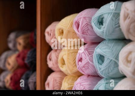 Balls of wool in various colors lie in a wooden cupboard in a shop. Narrow depth of field, focus on the pink spheres Stock Photo