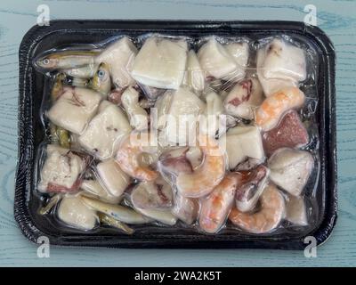 Mixed cleaned and cut fish ready for cooking in pieces frozen in vacuum sealed tray on blue wood bottom with clipping path included, top view Stock Photo