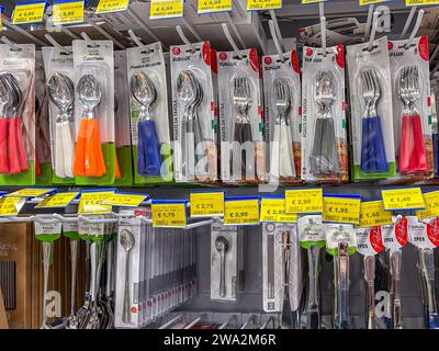 Italy - December 28, 2023: tableware with handles of various colors packaged and displayed for sale in Italian supermarket, spoons and forks and knive Stock Photo
