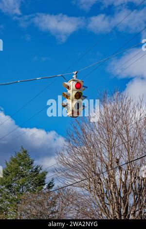 An old retro style traffic light with the red light illuminated still in use in a small rural town hanging by the wire in a intersection on a sunny da Stock Photo