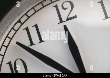 A clock with the hour hand pointing at twelve and the minute hand between 10 and 11. Close up. Stock Photo