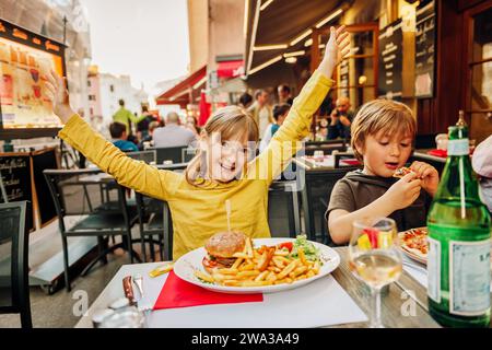 Happy kids eating hamburger with french fries and pizza in outdoor restaurant Stock Photo
