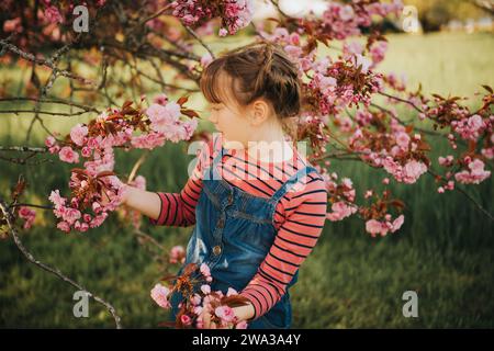 Outdoor spring portrait of a pretty little girl, standing between flowers of a japanese cherry in blossom Stock Photo