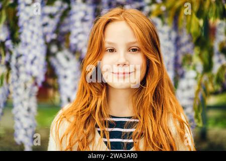 Close up portrait of adorable 9-10 year old red-haired kid girl posing in wisteria Stock Photo